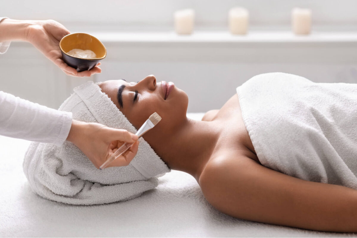 beautician holding bowl with face mask next to sleeping black lady