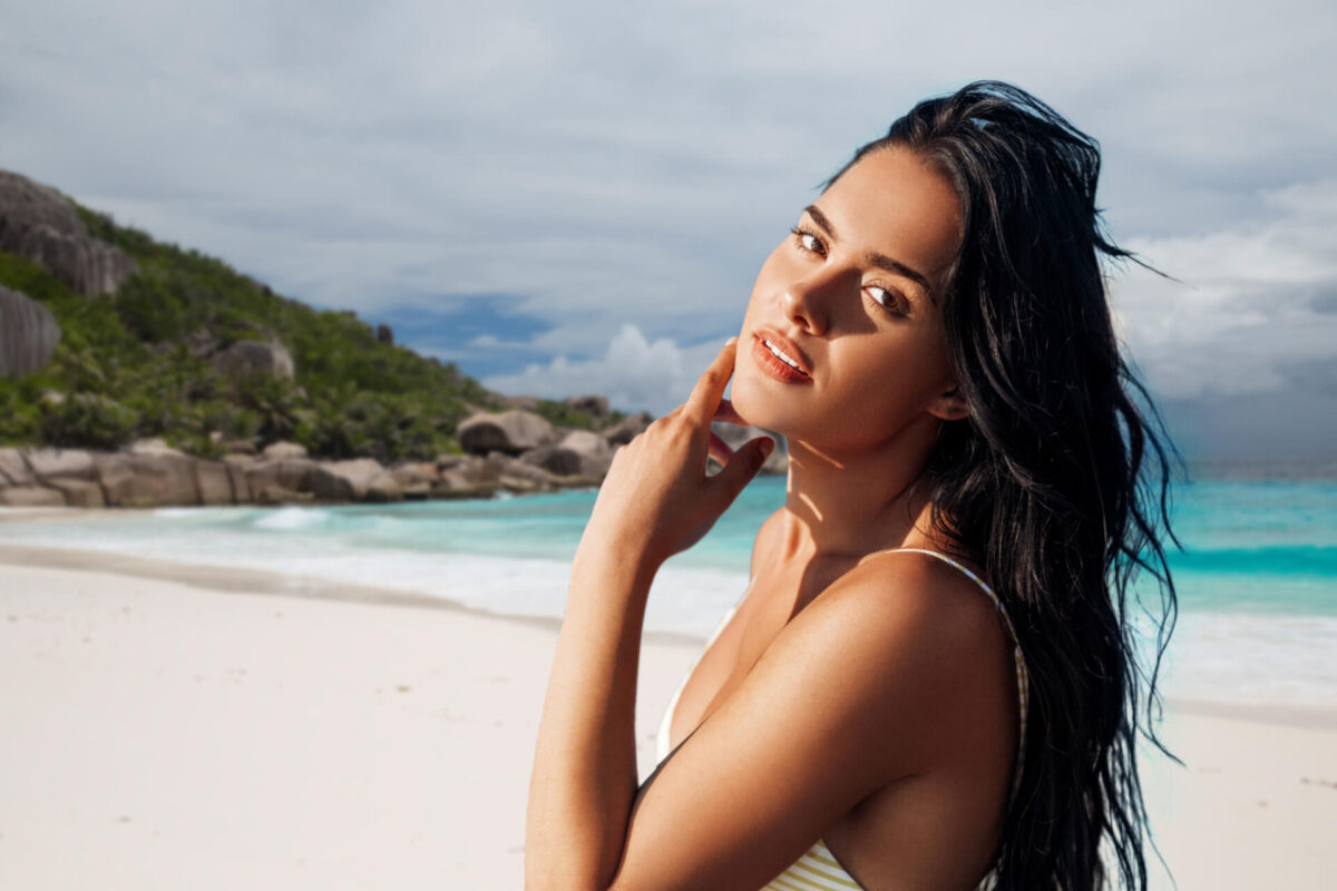 beautiful young woman in bikini swimsuit over tropical beach